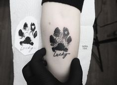 a black and white paw print tattoo on the left inner arm with words lucky written in cursive font