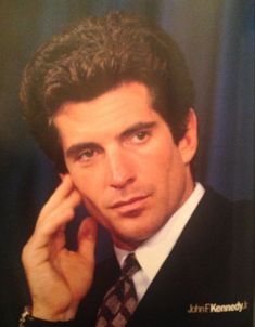 a close up of a person wearing a suit and tie holding his hand to his ear