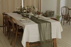 the table is set with white linens and flowers on it, along with two candles