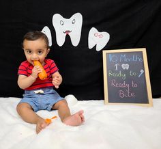 a small child sitting on a bed with a toothbrush in his mouth and a chalk board next to it