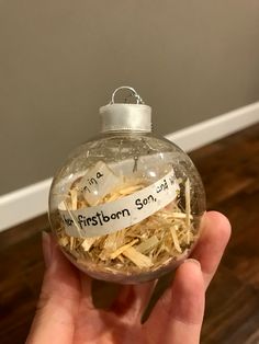 someone is holding up a glass ornament with shredded paper in it that says, firstborn son