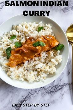 salmon curry on top of rice in a white bowl next to a gold fork and spoon