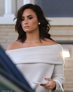 a woman in white off the shoulder sweater holding a cell phone and looking at something