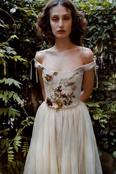 a woman standing in front of some plants wearing a dress with flowers on the waist