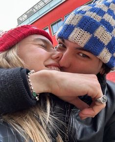 a man and woman kissing each other in front of a red building with a blue checkered hat on