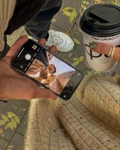 a person taking a photo with their cell phone next to a cup of coffee on the ground