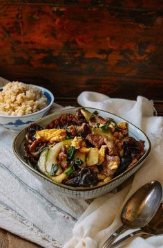 two bowls filled with food sitting on top of a white cloth next to silver spoons