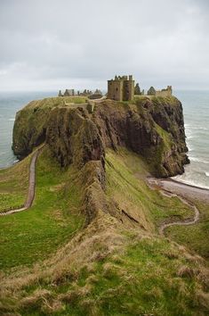 an old castle sitting on top of a green hill next to the ocean in scotland