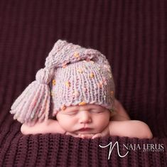 a baby wearing a knitted hat laying on top of a purple blanket