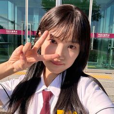 a girl in a school uniform is making the v sign with her fingers while standing outside an office building