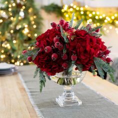 a vase filled with red flowers sitting on top of a table next to a christmas tree