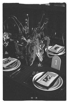 a black and white photo of a table setting with place settings, silverware, and flowers