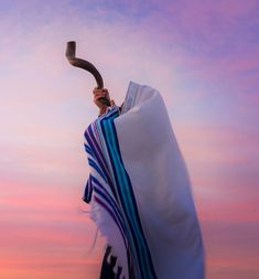 a person holding an object in their hand while standing under a colorful sky at sunset