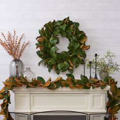 a fireplace with a wreath on top of it next to a fire place and vases