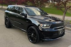 a black dodge suv parked on the side of the road next to some trees and bushes