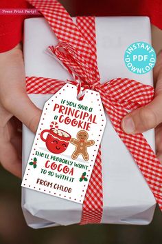 a person holding a gift wrapped in red and white paper with a gingerbread teacher's cookie on it