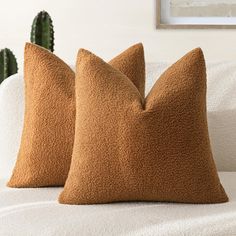 two brown pillows sitting on top of a white couch next to a green cactus plant