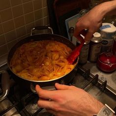 a man is cooking pasta in a pan on the stove with a red spatula