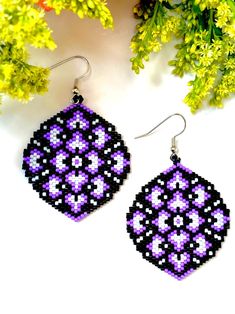 purple and black beaded earrings sitting on top of a table next to some flowers