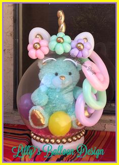 a blue teddy bear with balloons in it's mouth sitting on top of a table