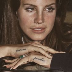 a woman with tattoos on her fingers and hand next to a car door window, looking at the camera