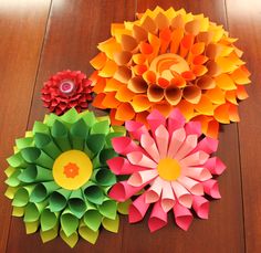 three different colored paper flowers sitting on top of a wooden table