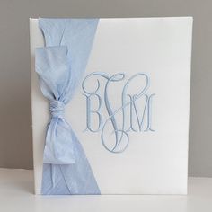 a white box with blue ribbon and monogrammed initials on it, sitting on a table