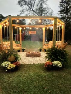 an outdoor fire pit surrounded by lawn chairs and plants with lights strung over the top