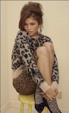 a woman sitting on top of a stool wearing leopard print sweater and high heeled shoes