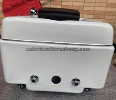 an old fashioned white refrigerator sitting on top of a metal table next to a brick wall