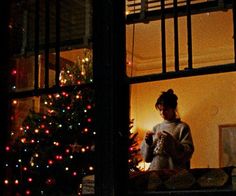 a woman standing in front of a christmas tree looking out the window at her cell phone