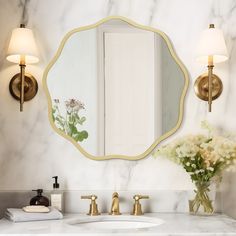 a bathroom with marble counter tops and gold fixtures, including a large round mirror over the sink