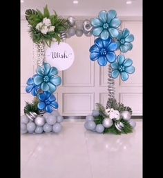 two blue and silver flowers are on display in front of a white wall with balloons