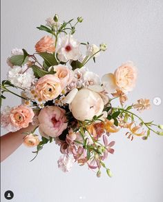 a person holding a bouquet of flowers in their hand with the background white and gray