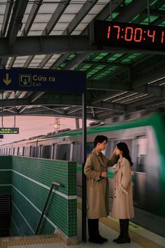 two people standing next to each other in front of a train at a subway station