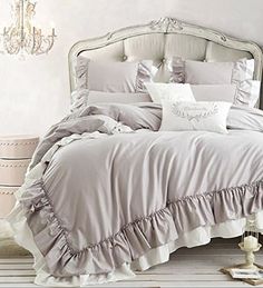 a bed with ruffled bedspread and pillows in a white room next to a chandelier