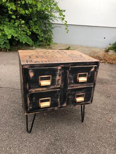 an old dresser is painted black and has gold pulls on the bottom, while it sits in front of some bushes