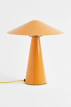 an orange table lamp sitting on top of a white floor next to a yellow cord