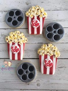 four cupcakes with popcorn on them and some cookies in the shape of film reel