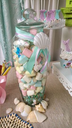 a glass jar filled with lots of candy and sea shells on top of a table