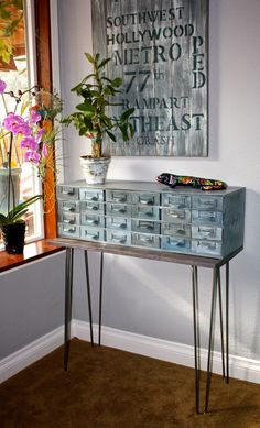 an old dresser with metal legs and drawers in front of a painting on the wall