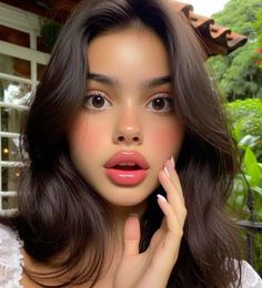 a woman with long brown hair and pink lipstick is posing for the camera while holding her hand to her face