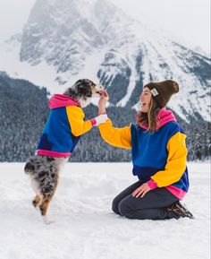 a woman kneeling in the snow petting a dog's nose with mountains in the background