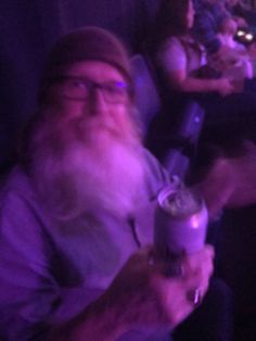 an old man with a long white beard holding a drink in his hand and looking at the camera