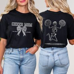 Get ready to cheer in style with this unique Front and Back Comfort Colors Shirt! The front features the words Cheer Mom in a collegiate font, adorned with a charming bow and the playful phrases very demure and very mindful on each side. But wait, the fun doesn't stop there - turn to the back of the shirt to find a large skeleton with pom-poms jumping for joy! This Cheer Mom Skeleton Comfort Colors Shirt is the perfect blend of funny and spooky, making it a must-have for any cheerleading mom. Wh Black Graphic Print Top For Cheerleading, Halloween Graphic Print Fan Apparel Tops, Black Top With Letter Print For Cheerleading, Black Crew Neck T-shirt For Cheerleading, Black Short Sleeve Tops For Cheerleading, Graphic Cotton Tee For Cheerleading, Cotton Graphic Tee For Cheerleading, Custom Print Cotton Tops For Cheerleading, Cotton Tops With Custom Print For Cheerleading