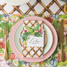 a place setting with pink plates, silverware and napkins on a floral table cloth