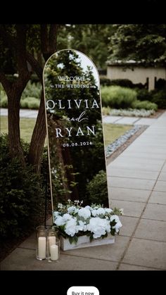 a wedding sign with flowers and candles on the side walk in front of a tree