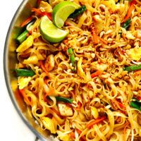 a pan full of noodles and vegetables with limes on the side for garnish