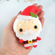 a hand holding a small christmas ornament with a santa clause on it's face