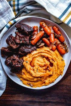 a white plate topped with meat, carrots and hummus next to mashed potatoes